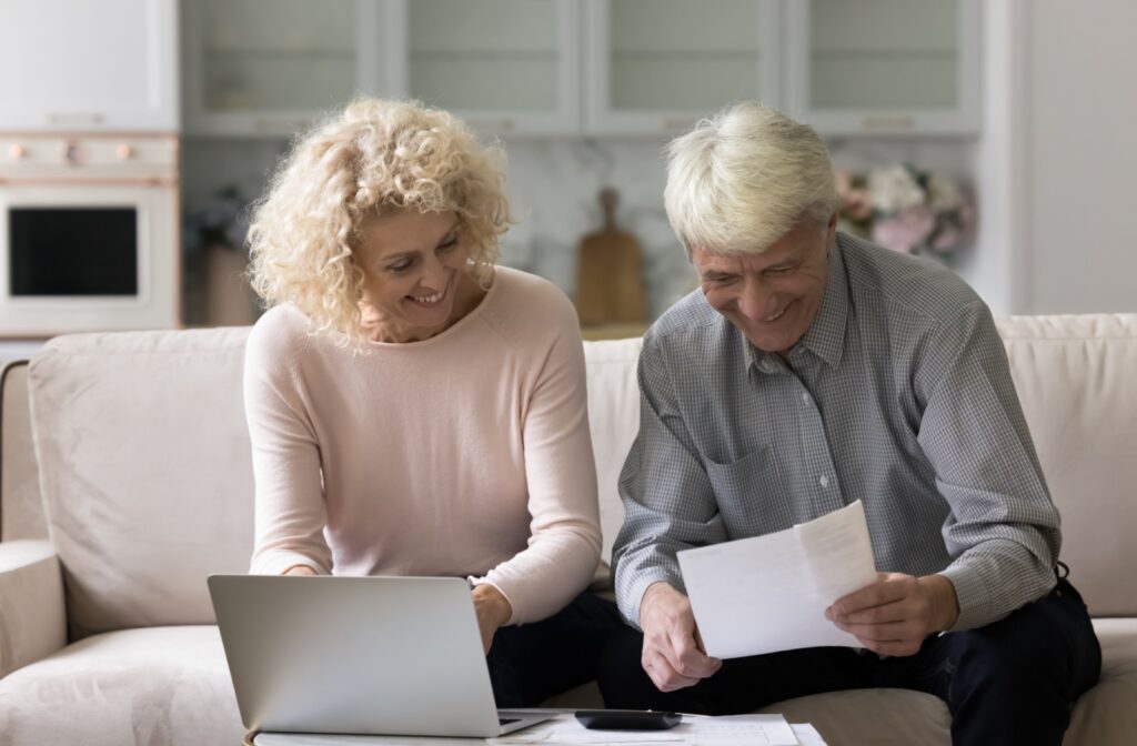An older couple with paperwork and a laptop, researching different retirement communities in their area.